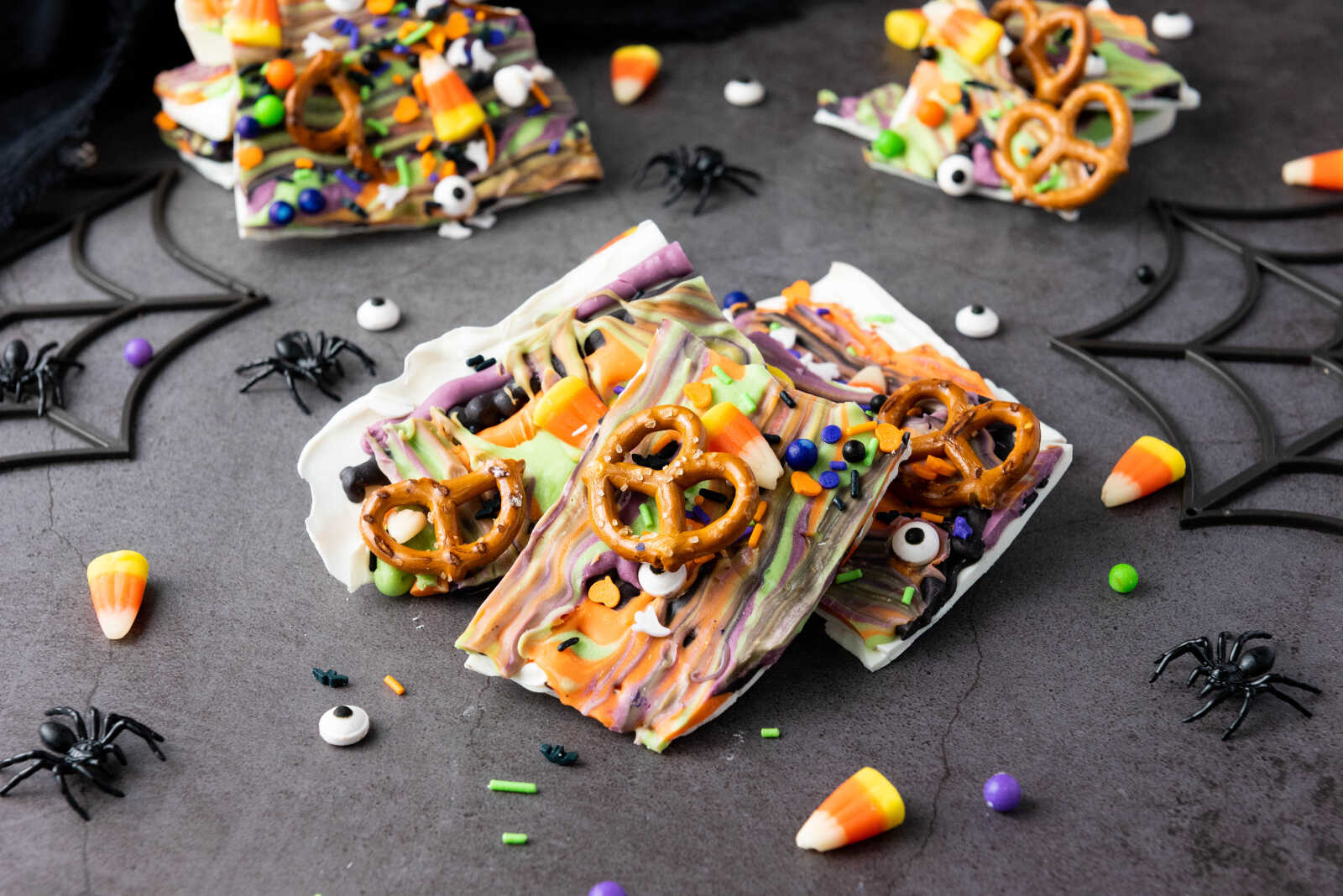 Halloween candy bark pieces with pretzels, candy corn, and sprinkles on a spooky decorated surface.