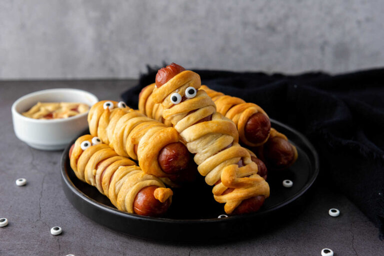 Air Fryer Halloween Mummy Hot Dogs with crescent dough and candy eyes on a black plate
